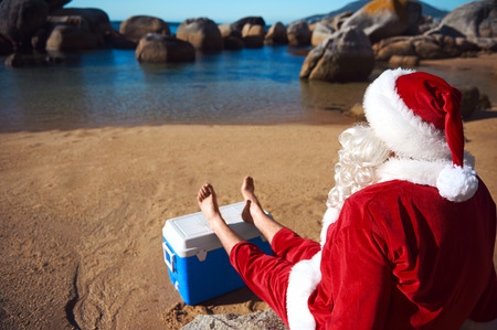 32308873 - father christmas relaxing on the beach resting his bare feet on his cooler while looking at the view