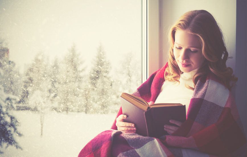 48969141 - happy girl reading a book by the window in the winter
