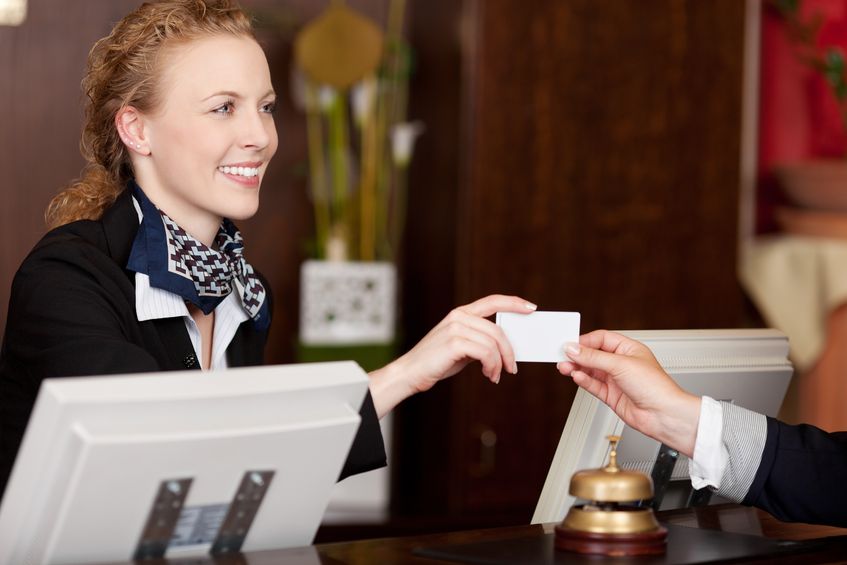 21375244 - smiling stylish beautiful receptionist handing over a blank white card to a client at the reception desk