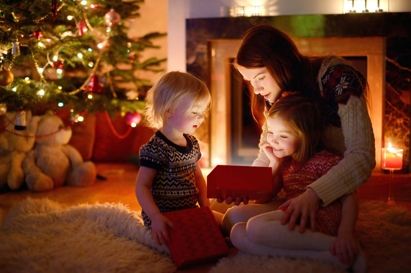 41117320 - young mother and her two little daughters opening a magical christmas gift by a christmas tree in cozy living room in winter