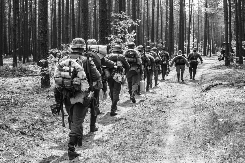 65313286 - unidentified re-enactors dressed as world war ii german soldiers walks on forest road. black and white photography