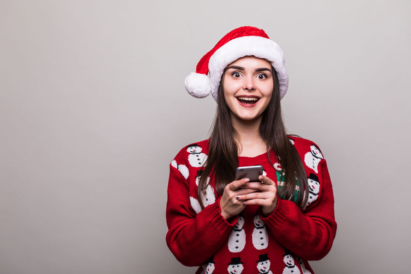 66503611 - beautiful girl model wear santa hat and christmas sweater text sms on phone on grey background