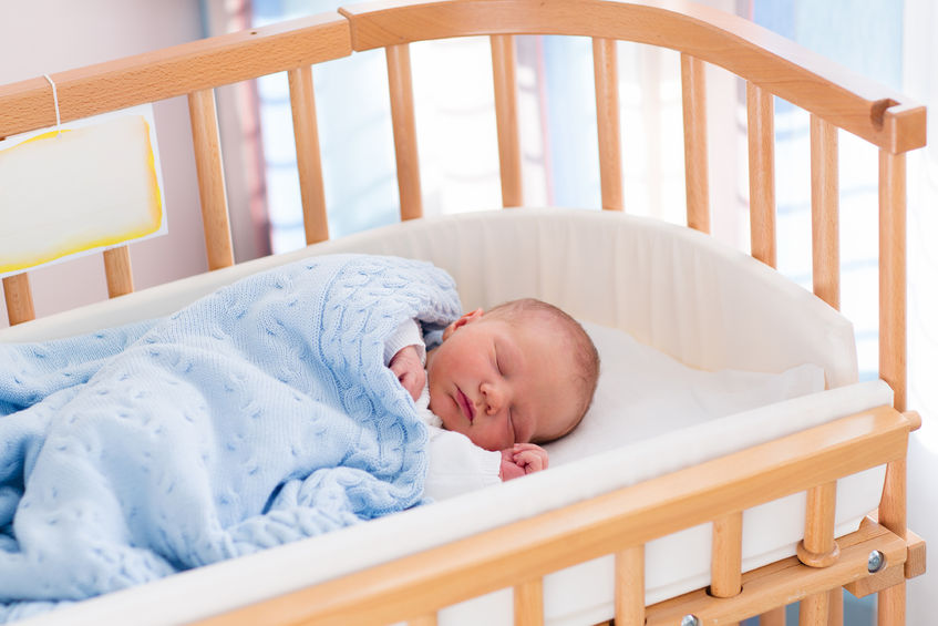 43359772 - newborn baby in hospital room. new born child in wooden co-sleeper crib. infant sleeping in bedside bassinet. safe co-sleeping in a bed side cot. little boy taking a nap under knitted blanket.