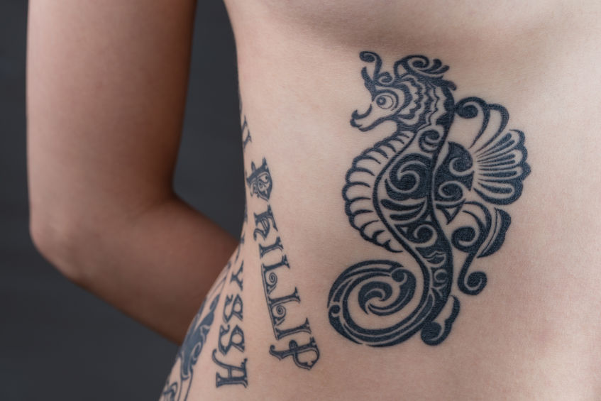 43679579 - a tattoo of a black tribal style seahorse with children's names wrapping around a woman's ribs.