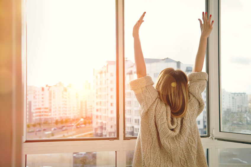 47462646 - woman near window raising hands facing the sunrise at morning