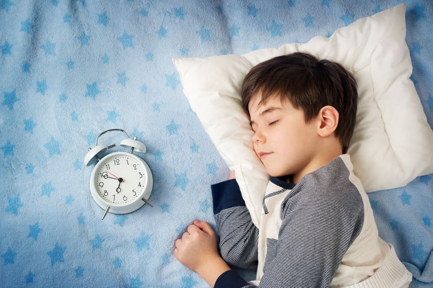 50431470 - six years old child sleeping in bed on pillow with alarm clock