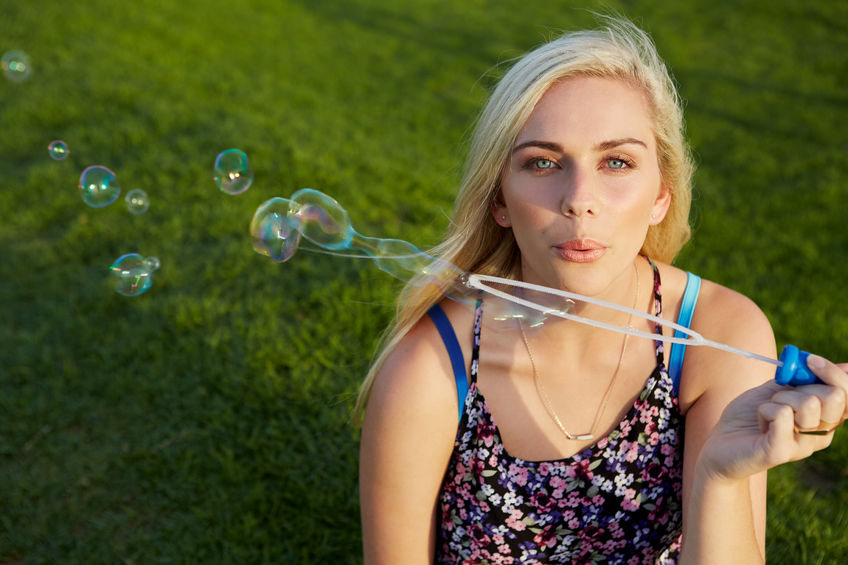 45974012 - attractive blonde woman blowing soap bubbles in park