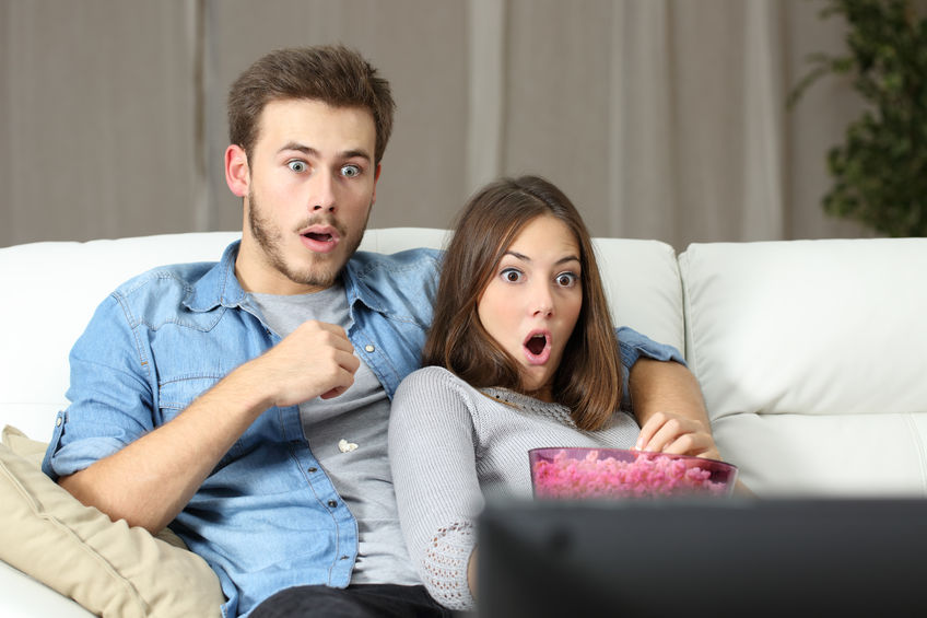 50532998 - amazed couple watching tv sitting on a couch at home