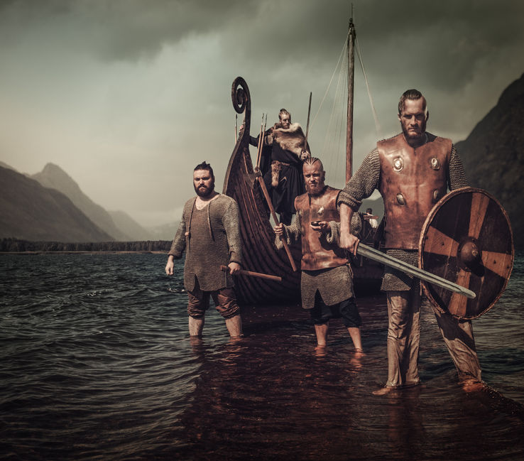 64798119 - armed, mad vikings warriors, standing on the seashore with drakkar on the background.