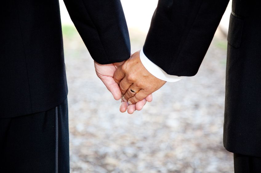 13626090 - closeup of a gay couple holding hands, wearing a wedding ring.  couple is a hispanic man and a caucasian man.