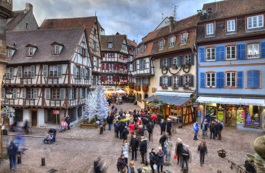 33361201 - colmar, france- decmebr 06,2013: people walking in a town square between traditional half-timber houses and specific christmas decoration in colmar, alsace, france. hdr image with selective motion blur on some of the people. colmar is considered to be the