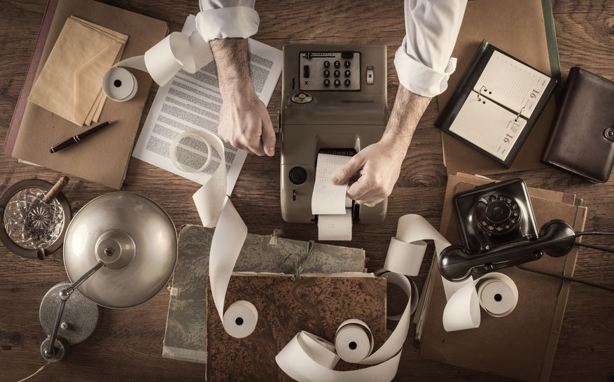 43569268 - messy vintage accountant's desktop with adding machine and paper rolls, he is working with the calculator