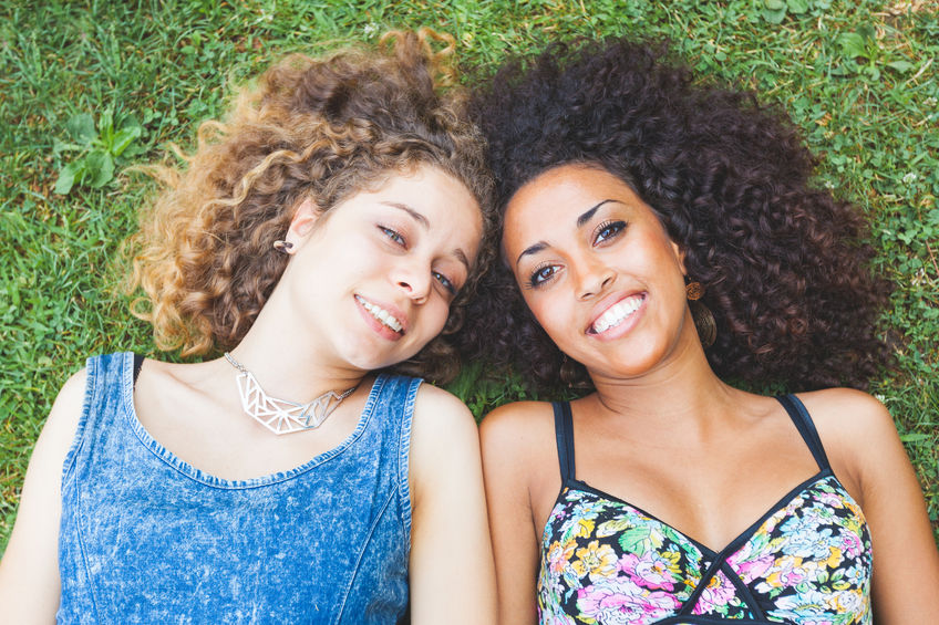 44119094 - a multiracial couple of women lying on the grass. they are two young women resting at park. one is caucasian blonde and the other is black brunette, both have curly hair. they are smiling and wearing summer clothes.