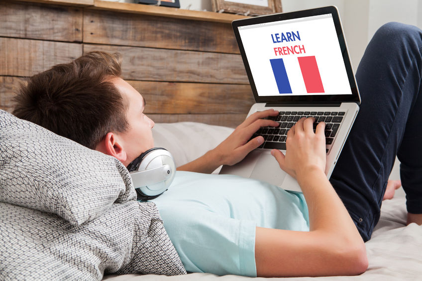 48616279 - young man using a laptop for learning french while lying in the bed at home.