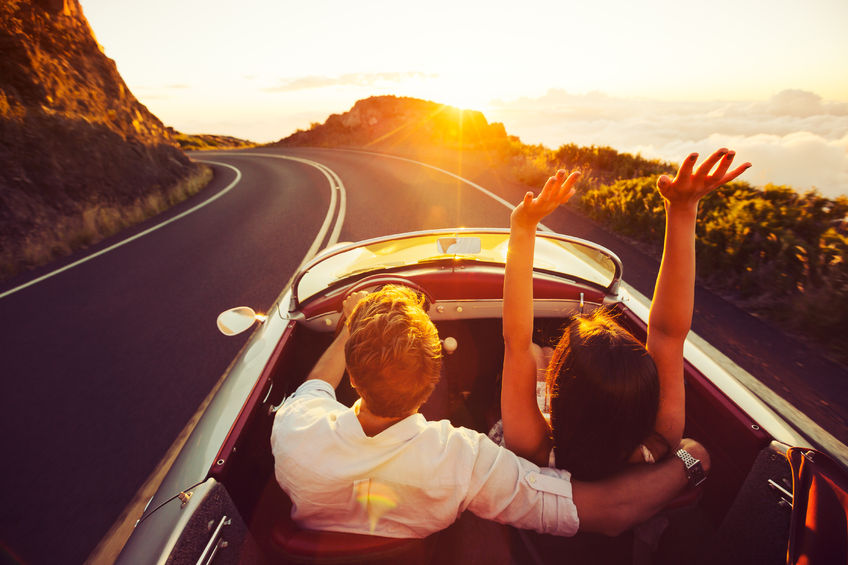 44181473 - happy couple driving on country road into the sunset in classic vintage sports car