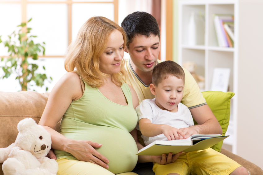 46065145 - happy parents - dad and pregnant mom reading book to child together on couch in home