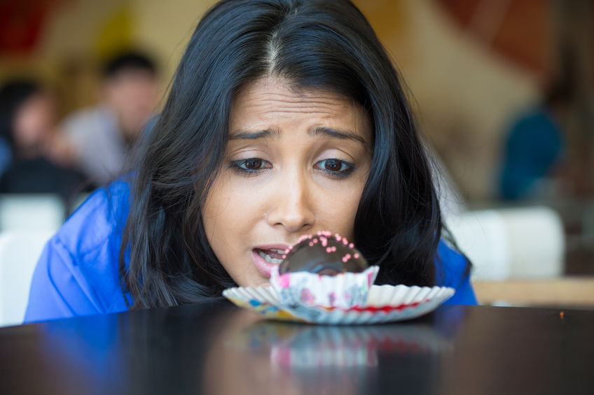51897791 - closeup portrait of desperate woman in blue shirt craving fudge with pink sprinkles dessert, eager to eat, isolated indoors background