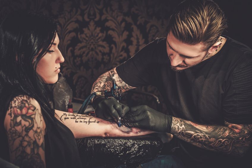 57069416 - professional tattoo artist makes a tattoo on a young girl's hand.