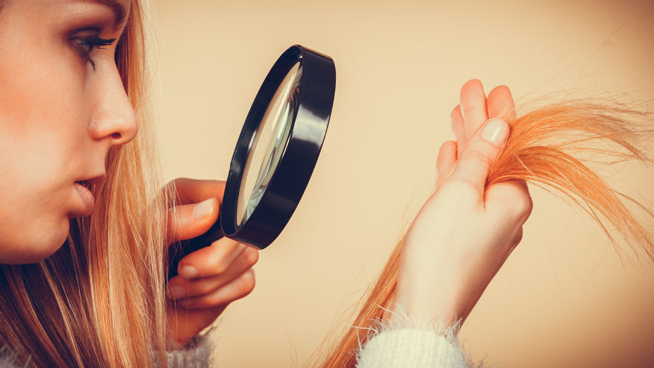70121172 - haircare, health problem concept. unhappy blonde woman looking at ends of her blonde hair through magnifying glass