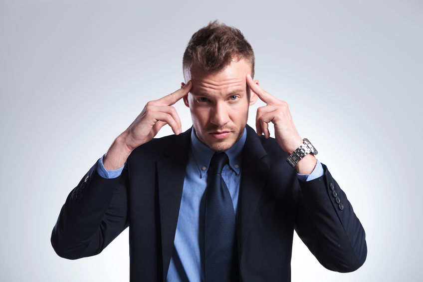 27837586 - young business man concentrating with his fingers at his temples while looking into the camera. on a light gray studio background