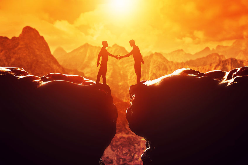 33643376 - two men shake hands over precipice between two rocky mountains at sunset. business, deal, handshake, connection concepts