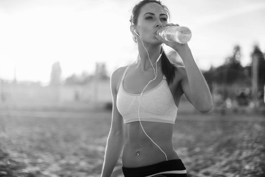 43880602 - beautiful fitness athlete woman resting drinking water after work out exercising on beach summer evening in sunny sunshine outdoor portrait.