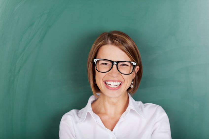 21148080 - laughing woman wearing glasses and standing in font of a class blackboard