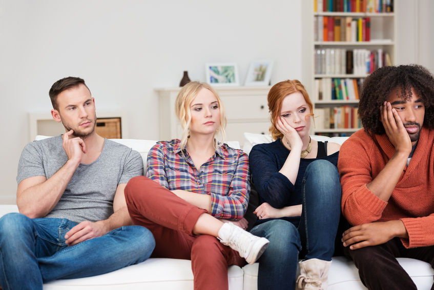 29143734 - bored group of multiracial friends relaxing at home sitting in a row on a comfortable sofa watching something off screen to the right with glum expressions